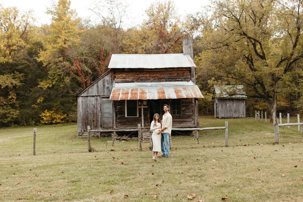 Historic log cabins with rustic wooden porches line a grassy field during fall.