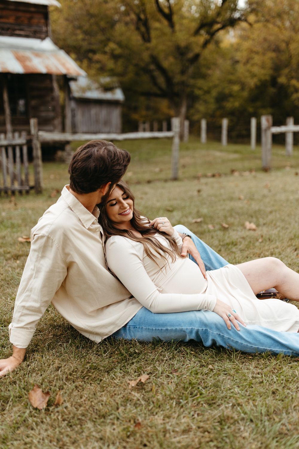 Couple lying together on autumn grass in front of rustic cabin setting.