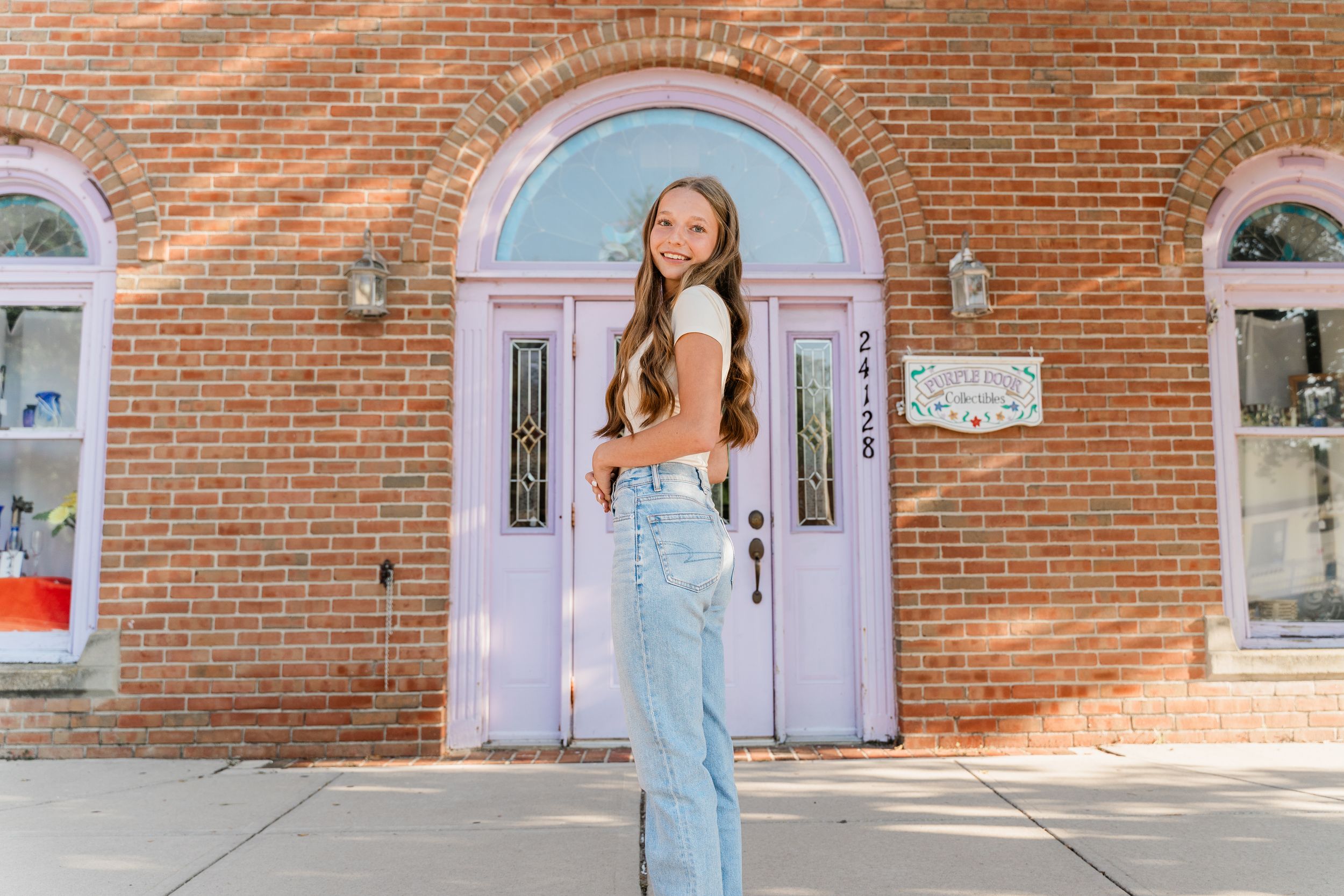 A woman in a blue dress poses in front of a brick wall with a pink door.