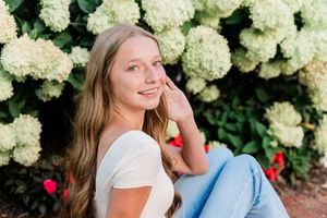 A bright outdoor portrait session featuring white hydrangea bushes in full bloom creating a lush natural backdrop.