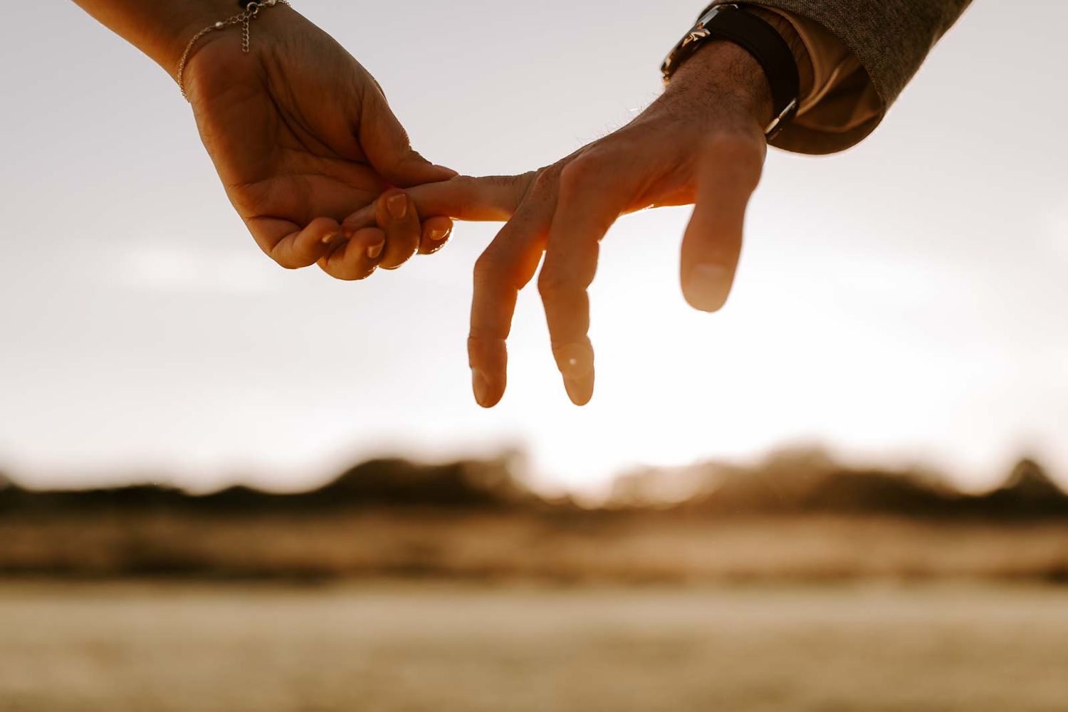 Silhouetted hands join together against a bright sunset sky in a gesture of unity and connection.
