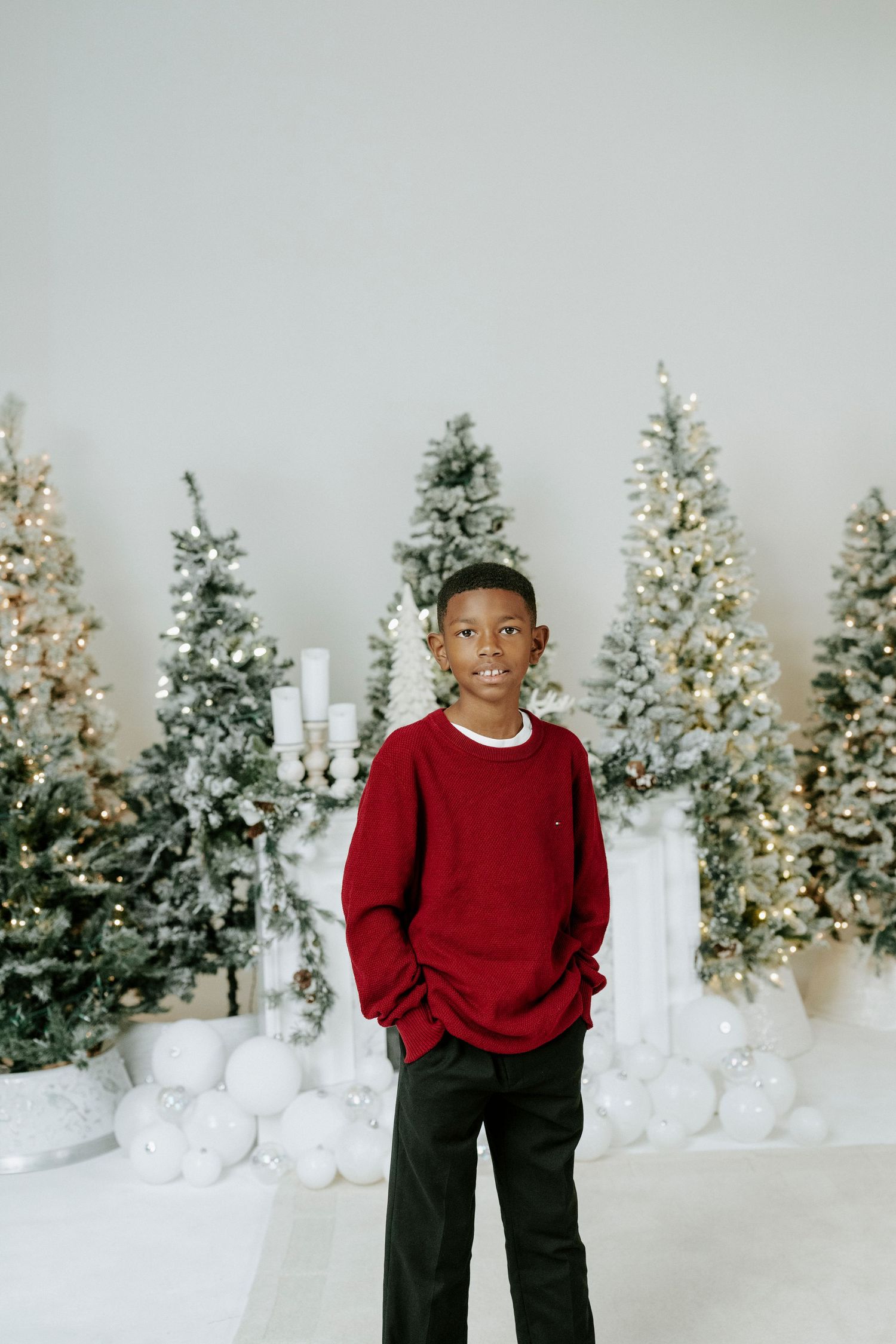 A festive holiday photo session setup with illuminated Christmas trees and white decorative elements in the background.