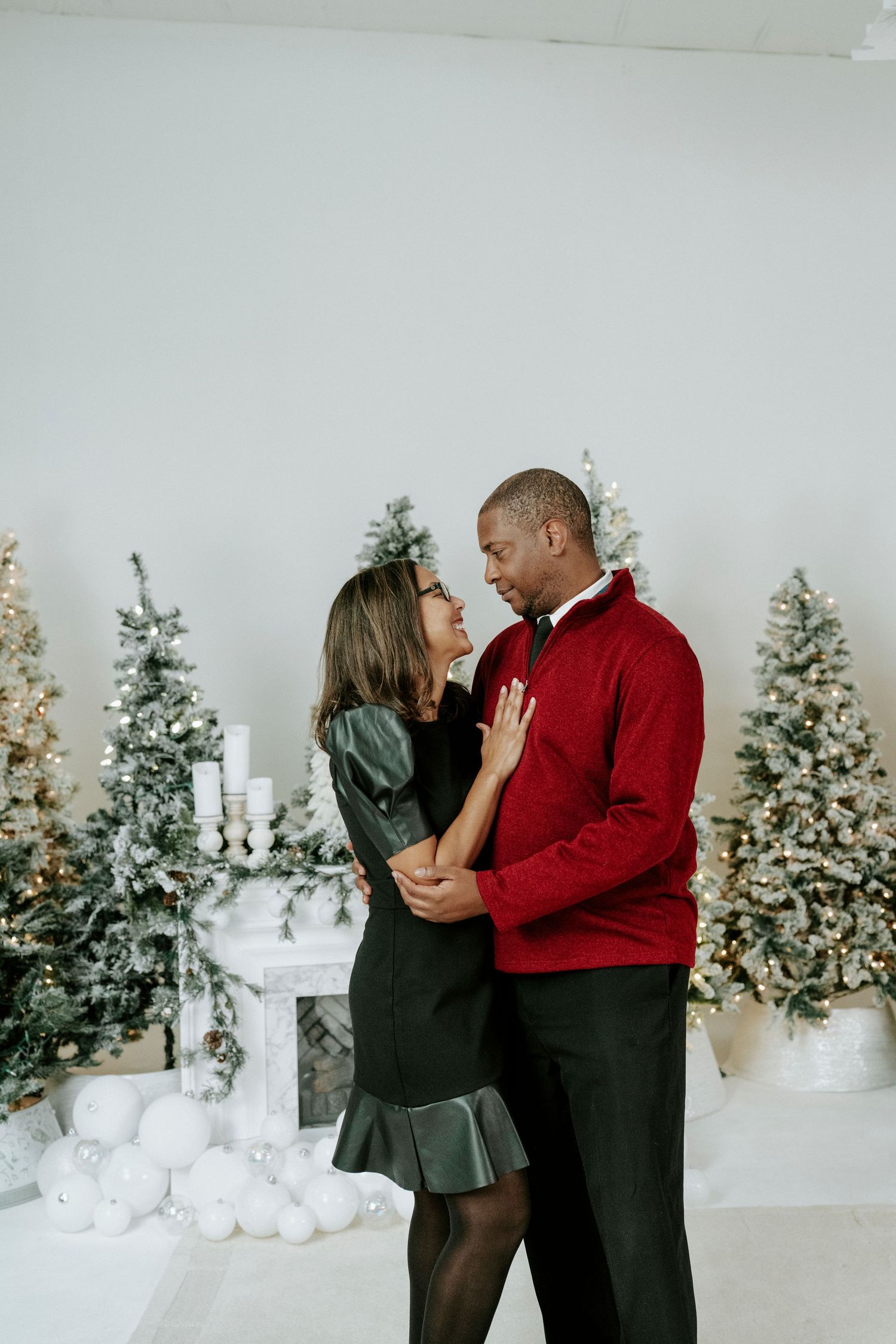 A couple shares an intimate moment in front of decorated Christmas trees and winter decor.