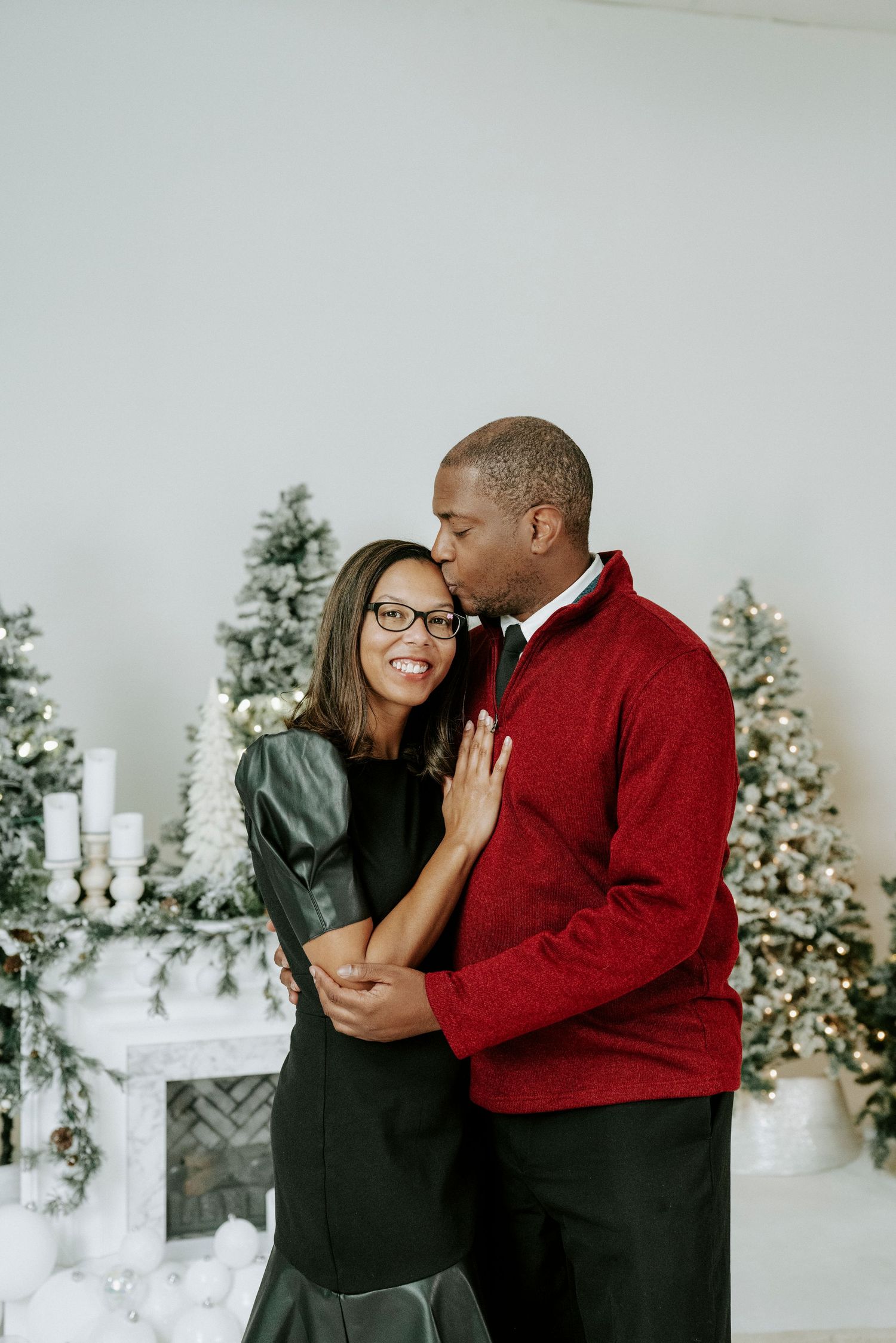 Couple in winter holiday setting sharing intimate moments with decorated Christmas trees in background.