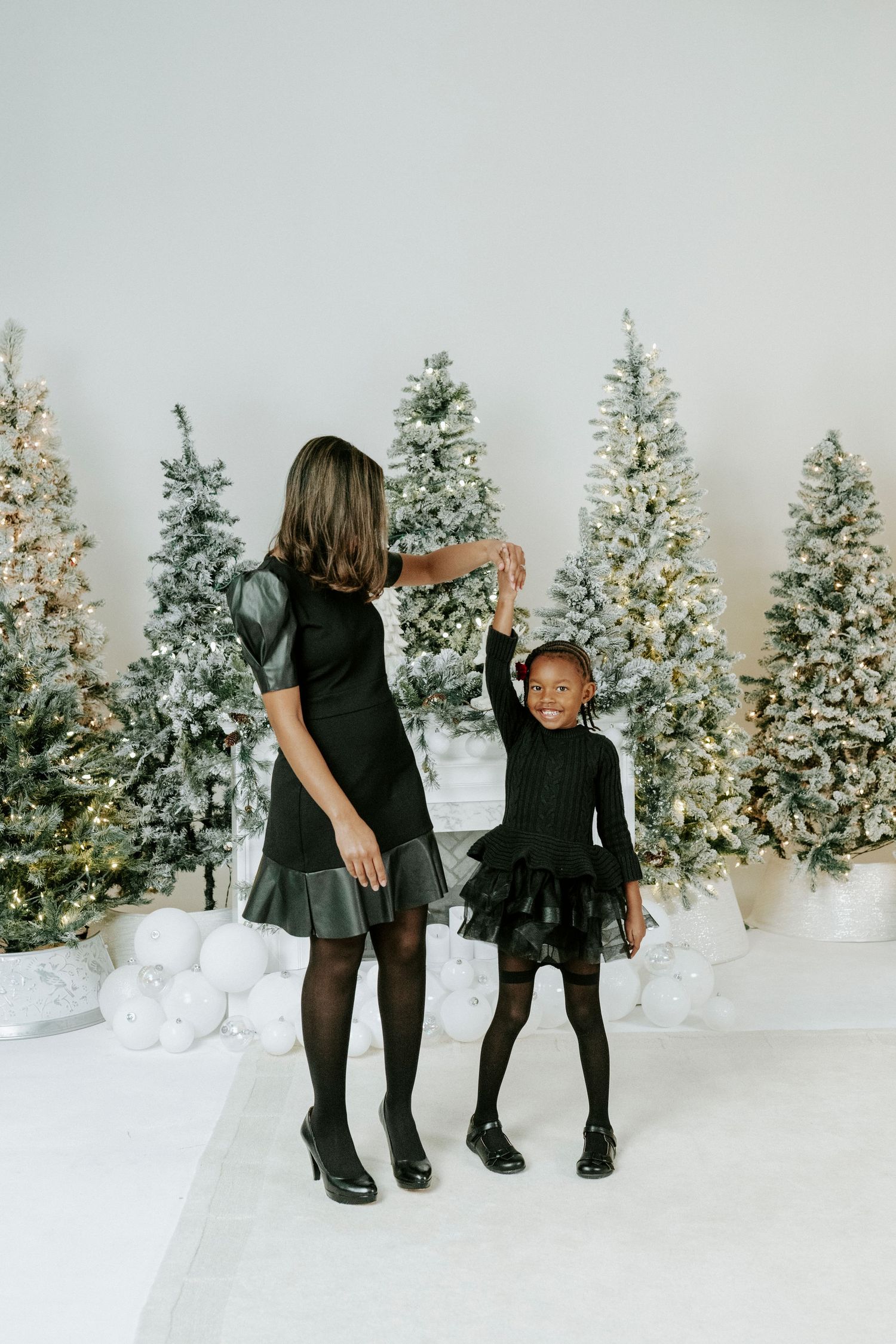 A series of holiday photos showing two people in black outfits posing playfully in front of decorated Christmas trees.