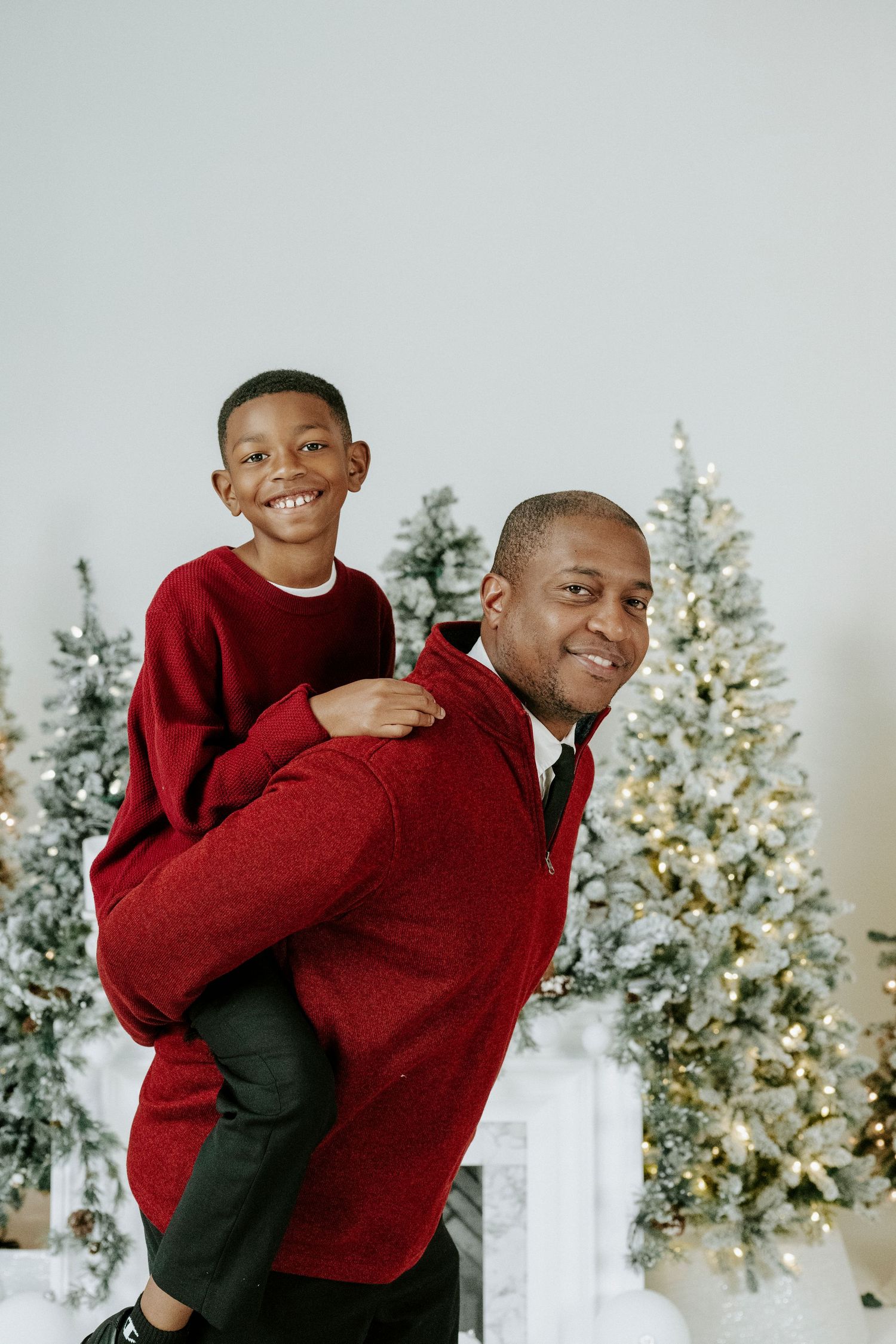 A playful holiday photoshoot with red sweaters and decorated Christmas trees in the background.