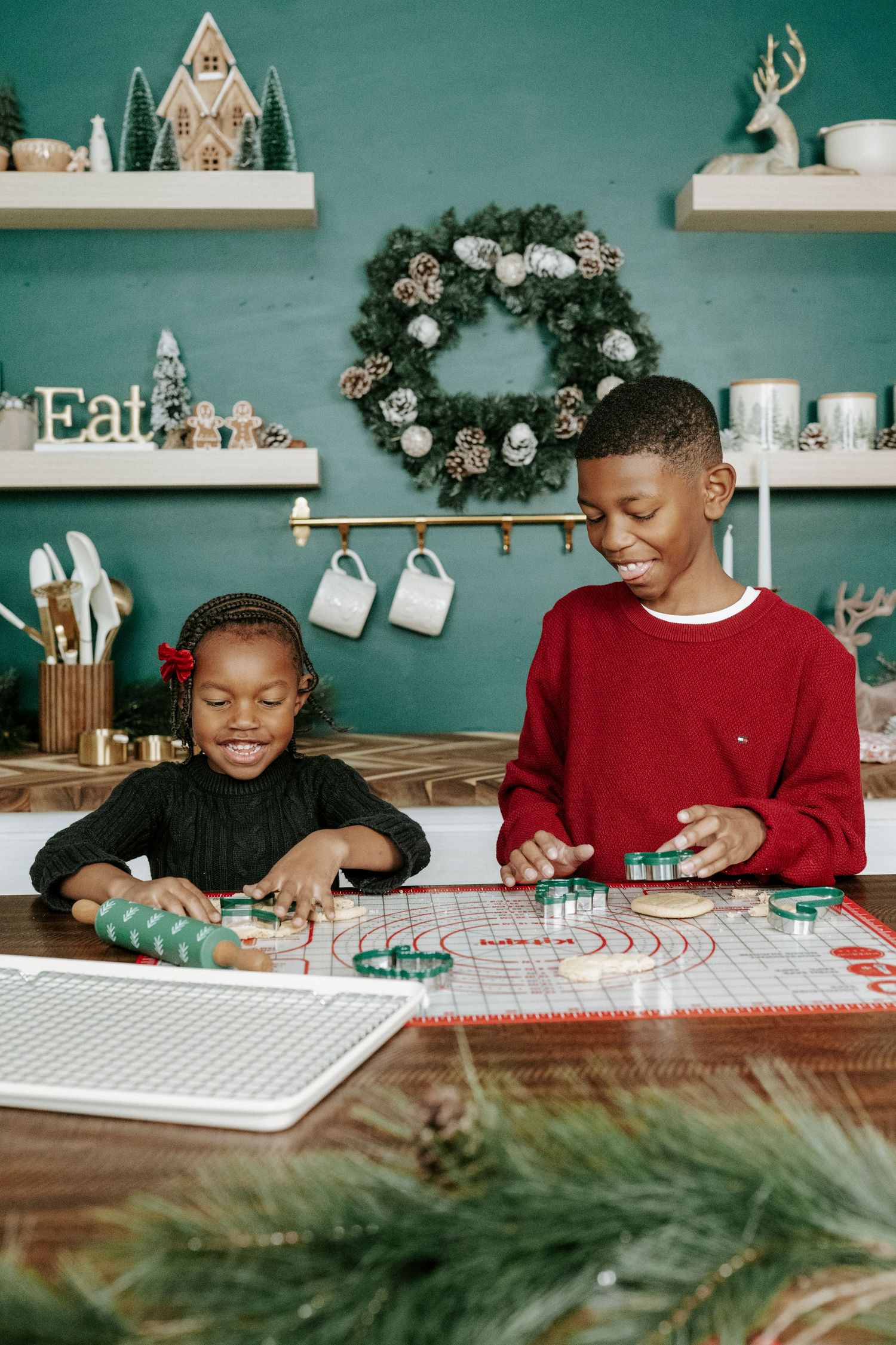 Two people working together on holiday crafts and wrapping paper at a wooden table with festive decorations.