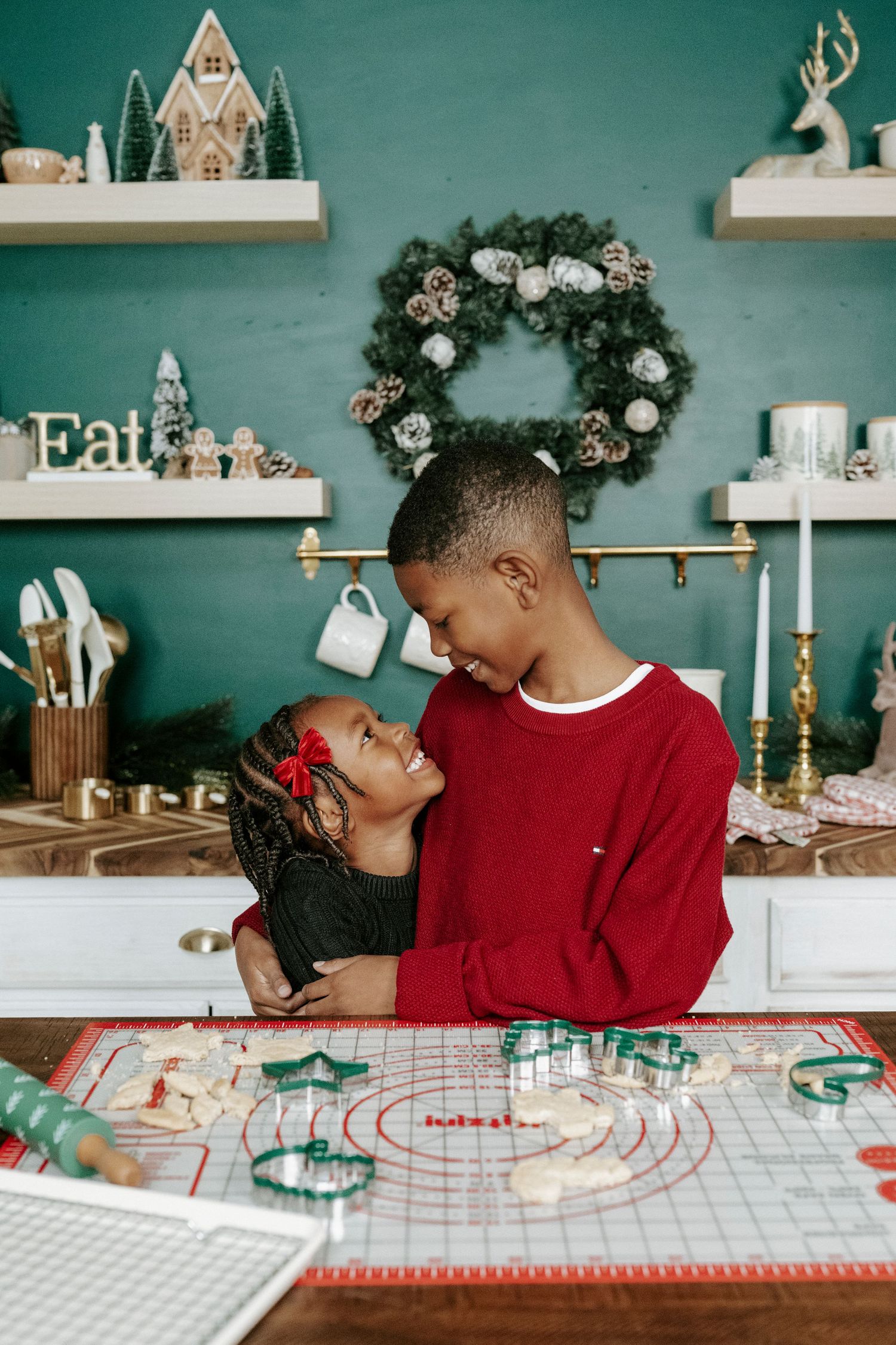 A couple shares playful moments while baking in a kitchen with teal walls and holiday decorations.