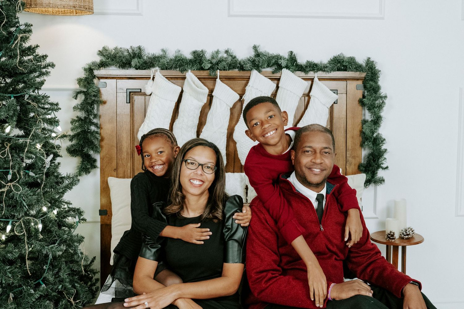 A joyful family wearing coordinated red and black outfits poses together for holiday portraits against a winter backdrop.