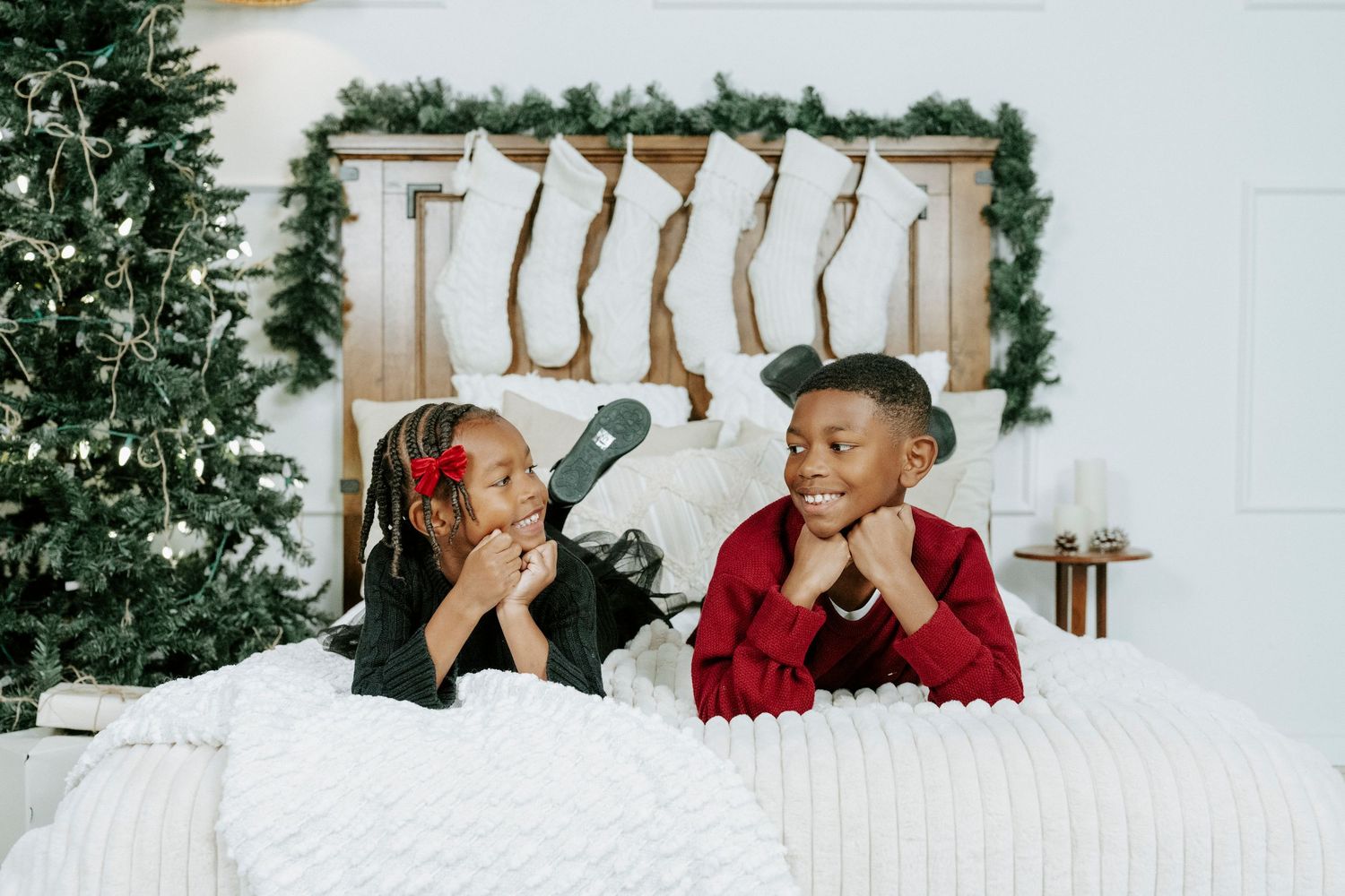 A festive holiday scene with two people posing playfully in front of a Christmas tree and white backdrop.