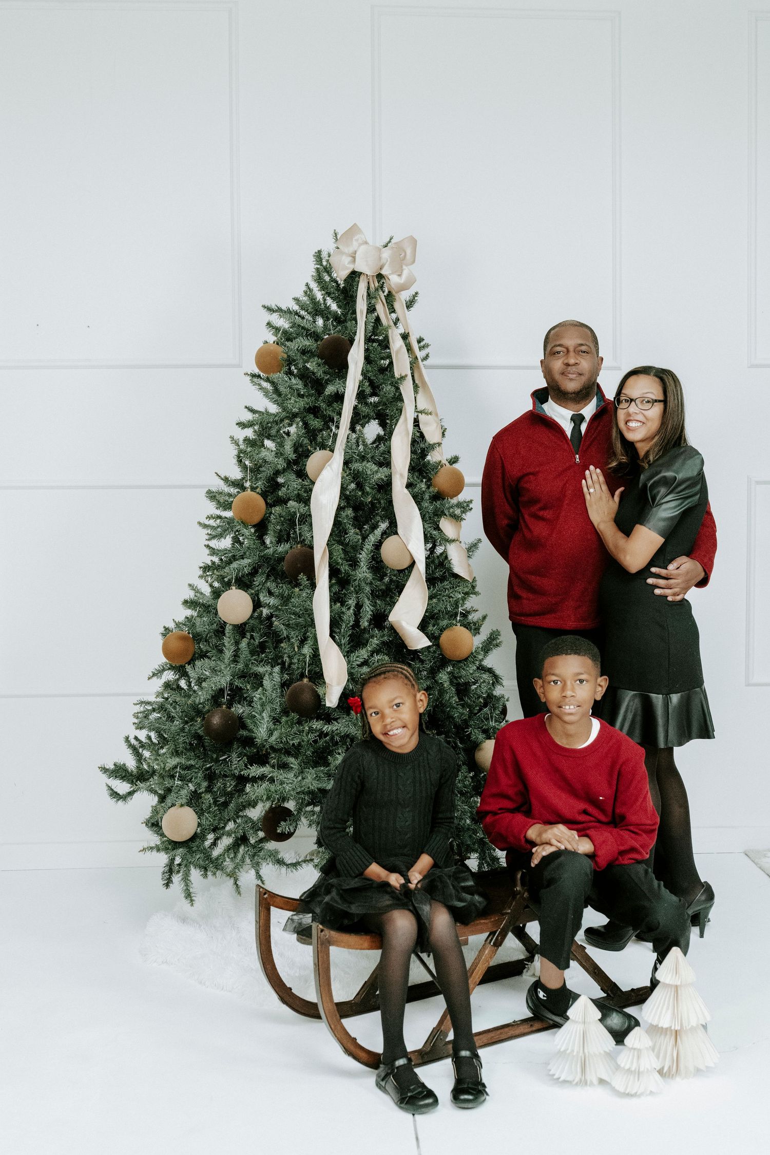 A family poses for a holiday portrait in front of a decorated Christmas tree with a vintage wooden sleigh.