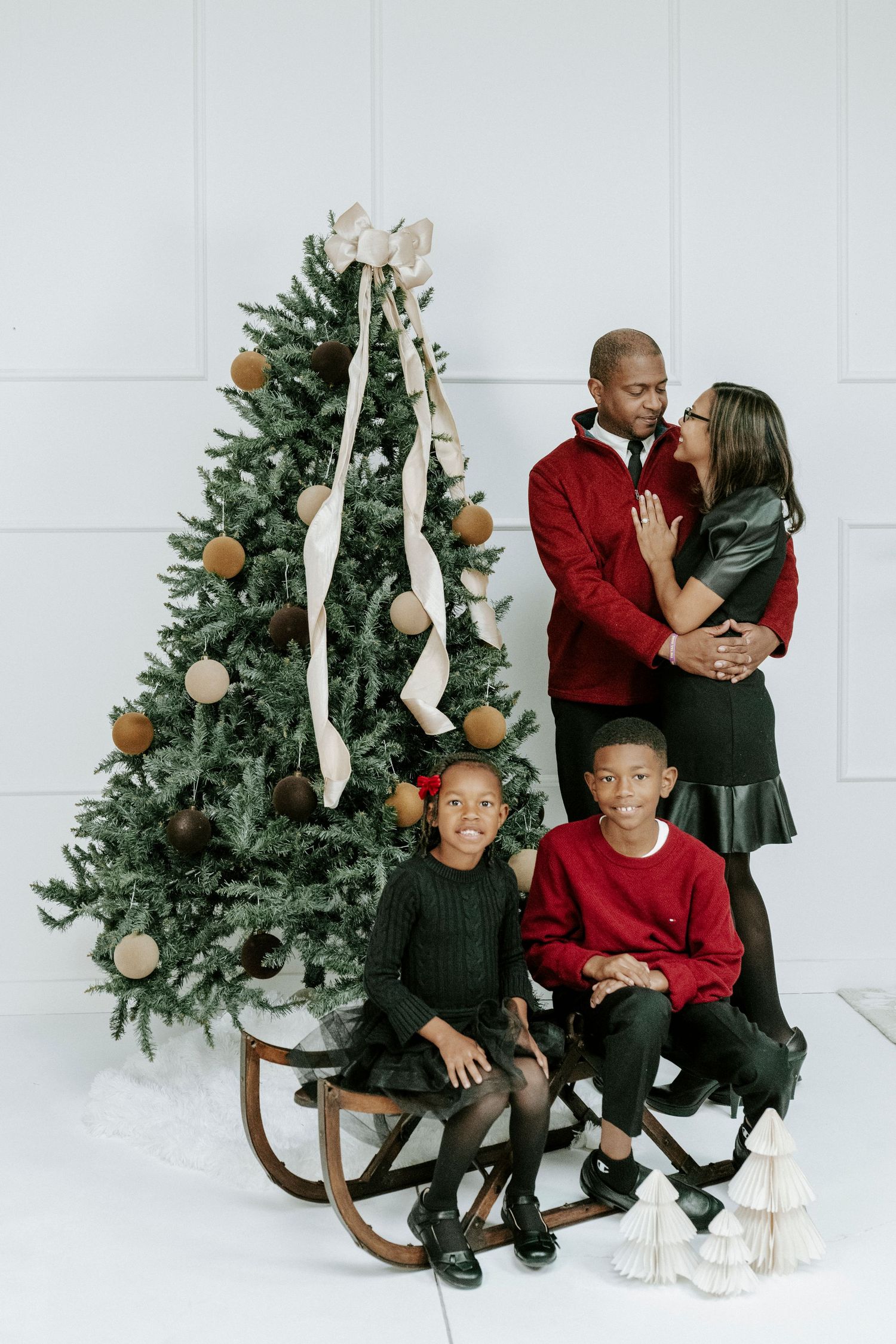 Festive family portrait session with coordinated red and black outfits by decorated Christmas trees.