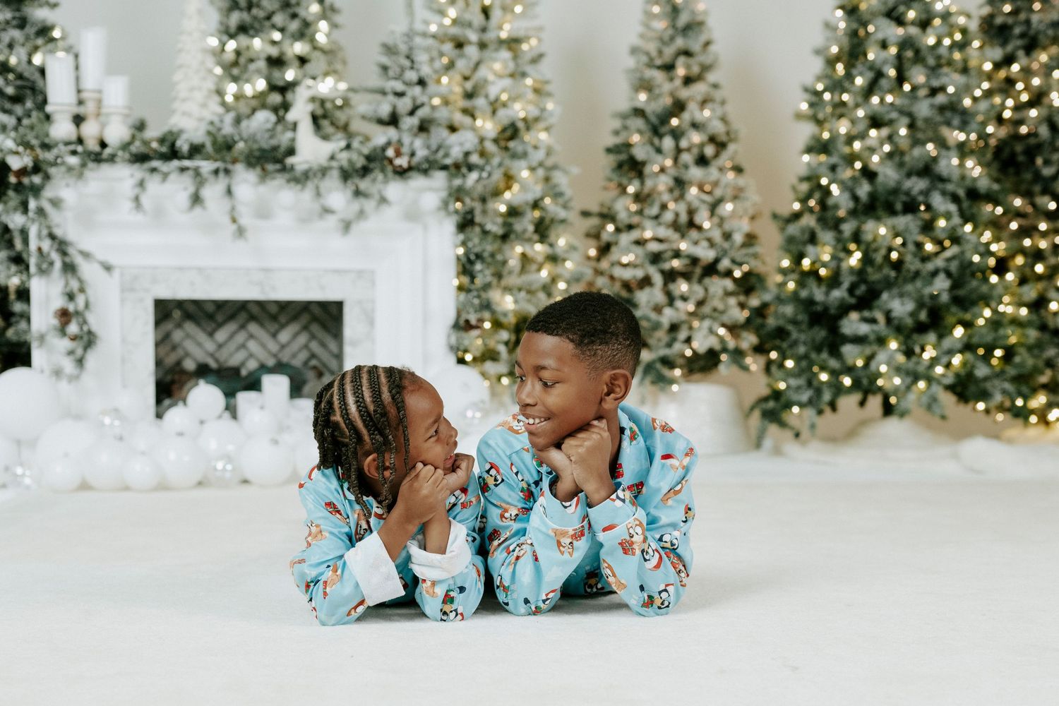 A couple in matching blue floral outfits shares intimate moments in front of decorated Christmas trees and snow.