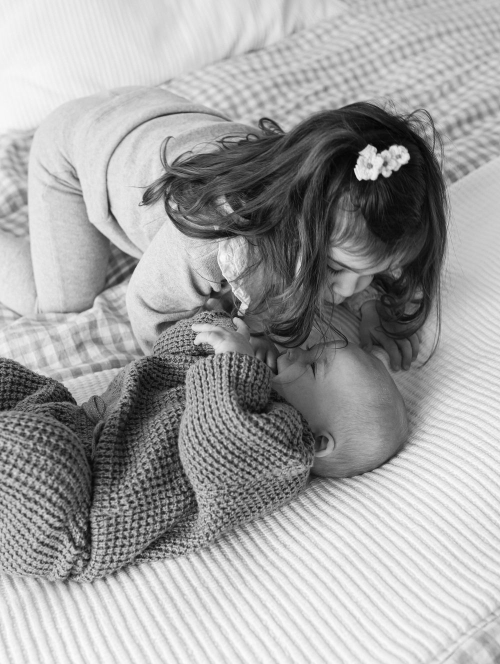 A tender black and white moment captured on a striped bed with a knit blanket, showing gentle affection and care.