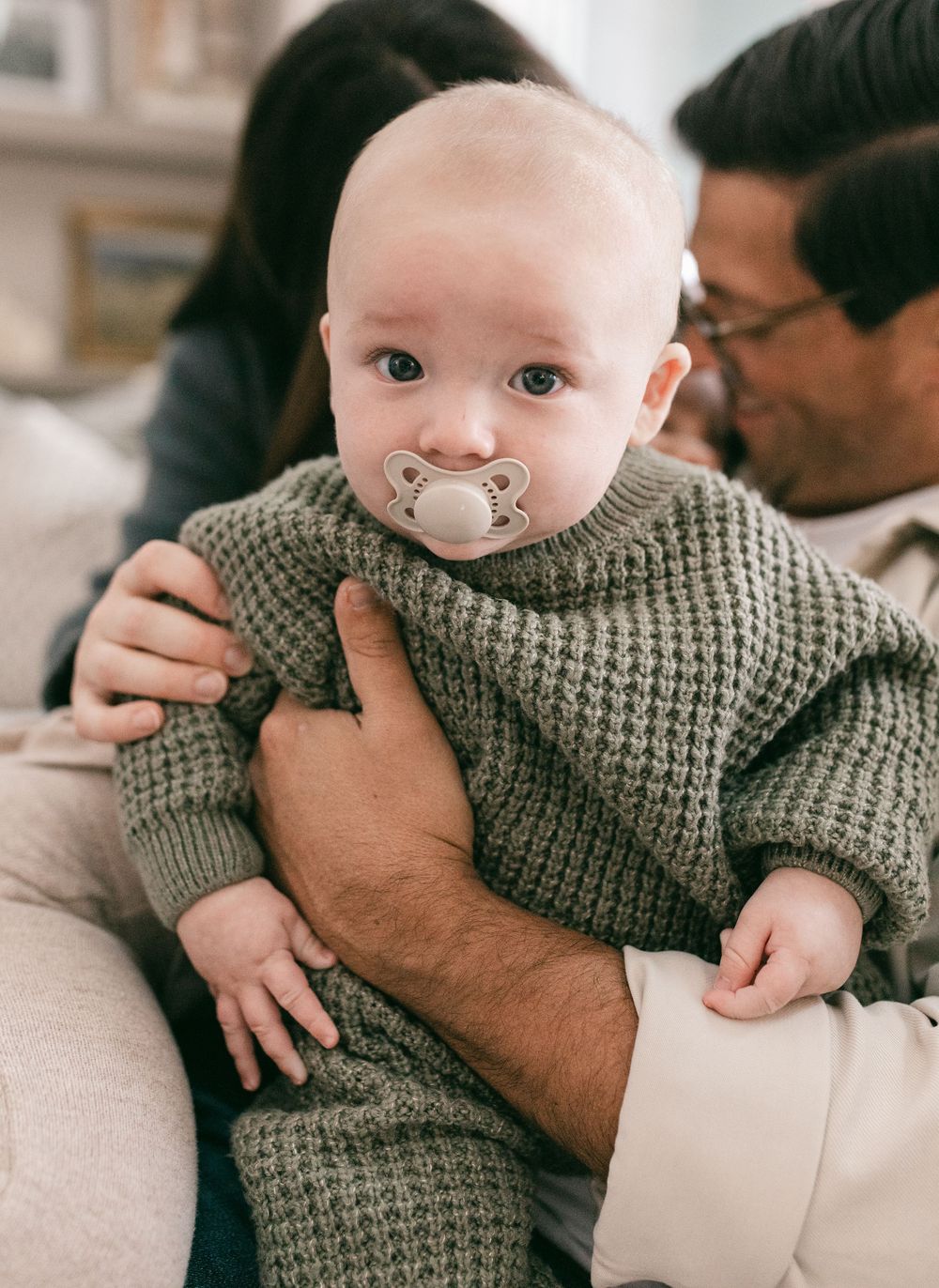 A baby in a gray knit sweater is held and lovingly embraced in a series of tender moments.