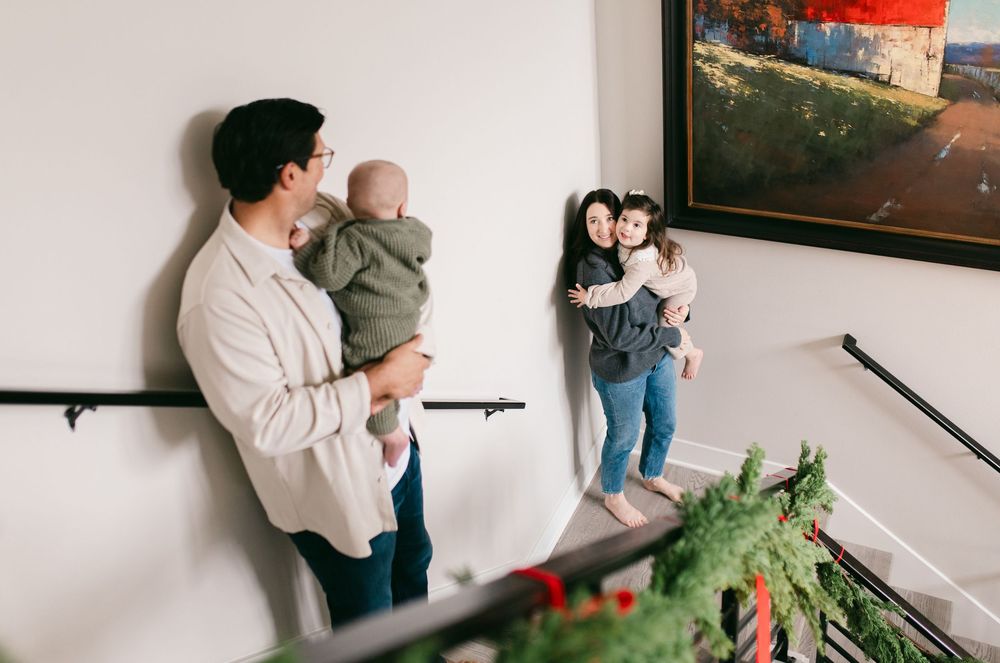A couple embraces in a cozy indoor setting with natural window light streaming in.
