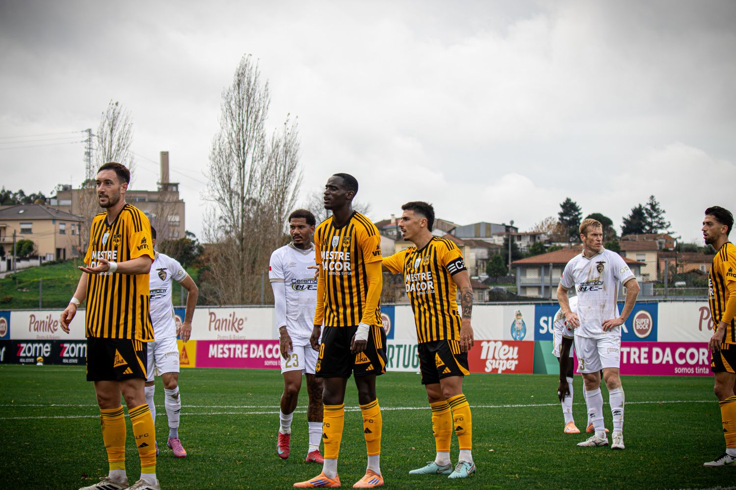 Soccer players in yellow and black striped jerseys walking on a field with advertising boards visible.