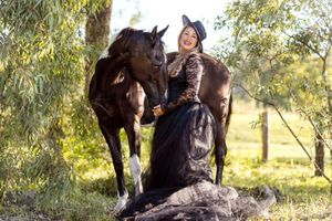 A black white horse and person stand together in a sunlit field with trees in the background during a photoshoot in Sydney with a horse