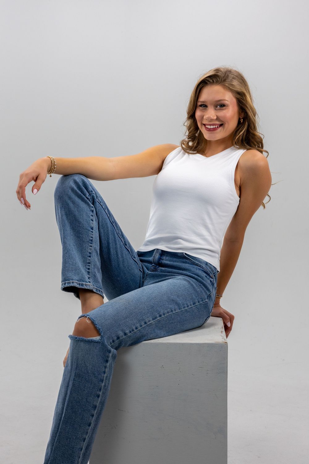 Fashion model in white tank top and blue jeans poses casually against grey backdrop in multiple poses.