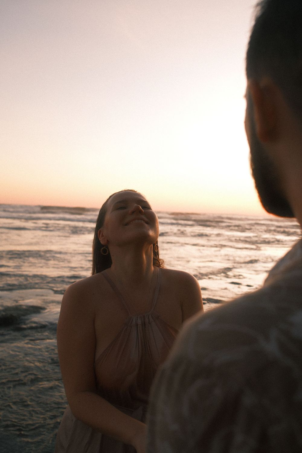 Intimate couple moment captured during sunset at beach with waves in background.