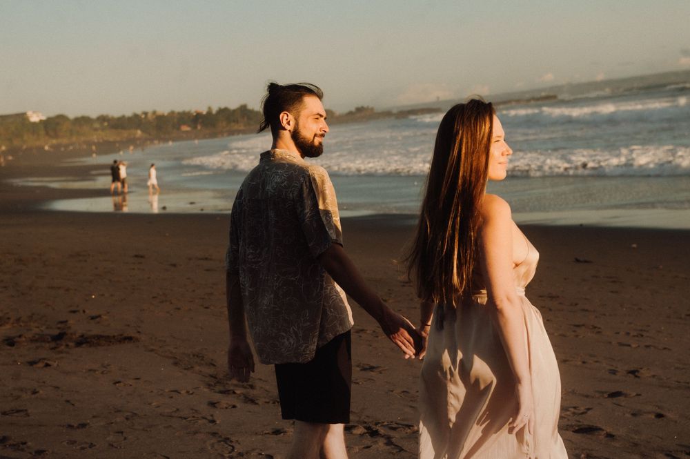 A couple walks along a misty beach at sunset holding hands and embracing.