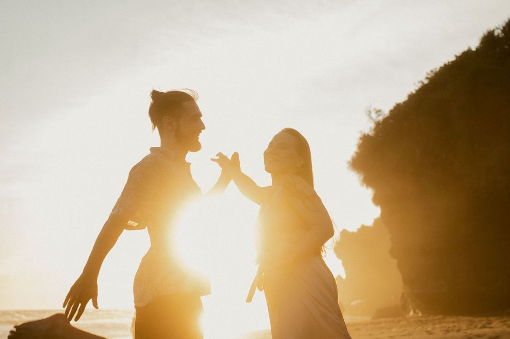 Silhouettes of a couple against a bright setting sun on a beach.