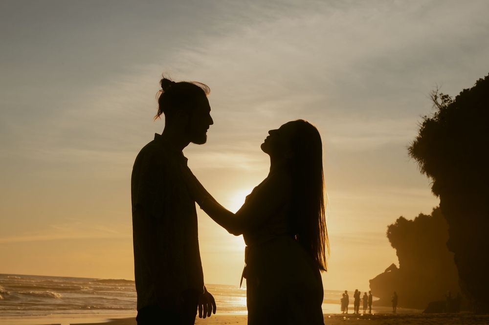 Silhouettes of people standing together against a dramatic sunset sky at the beach.