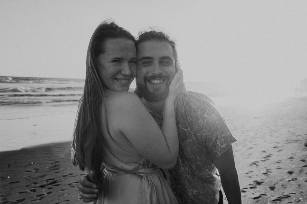 Happy couple sharing intimate moment on beach with ocean waves behind them.