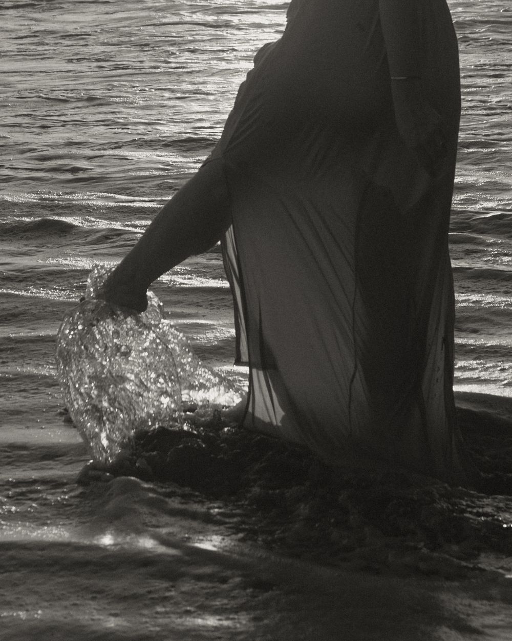 Person in flowing dress splashing in ocean waves at sunset.