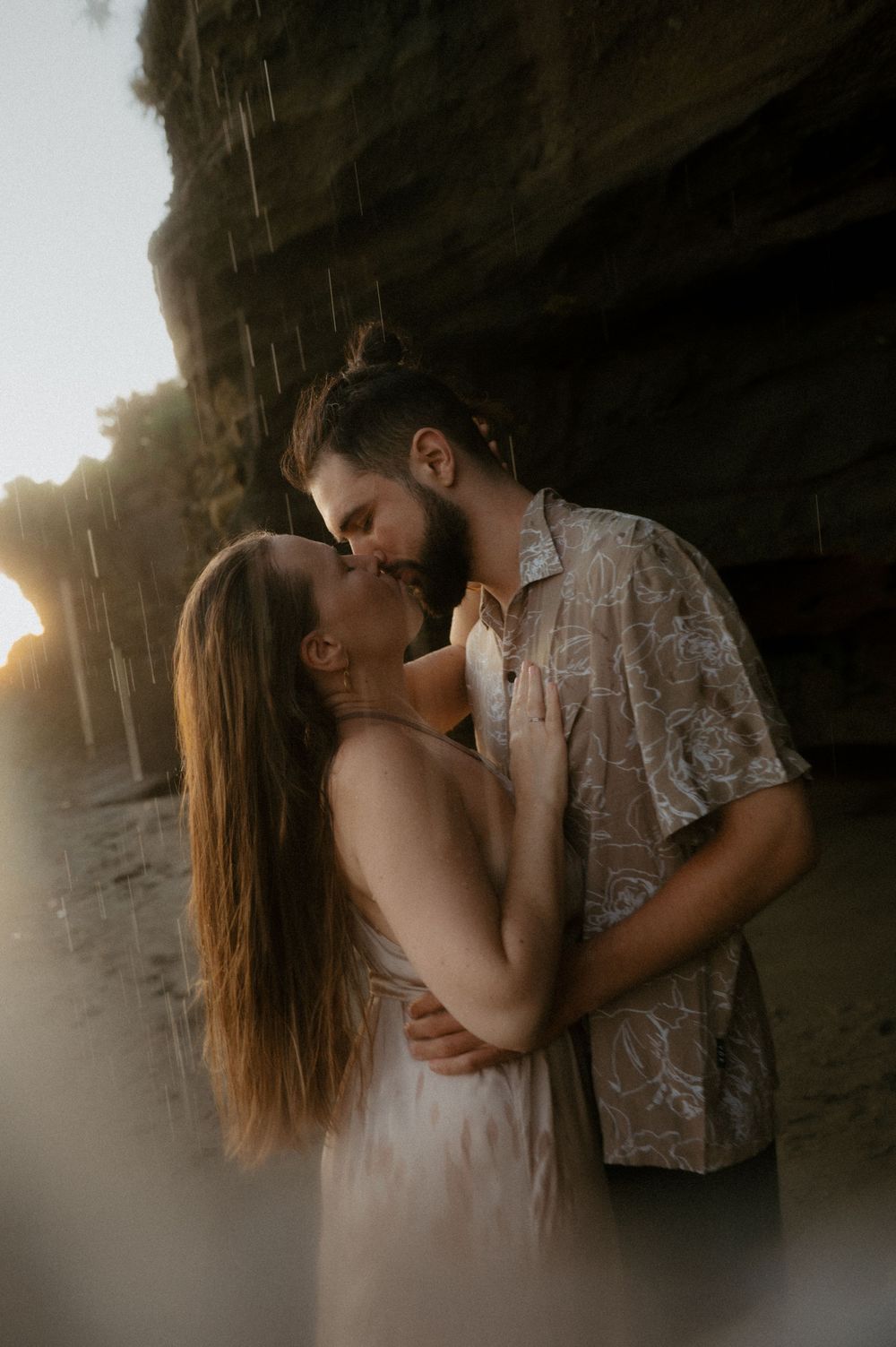 Couple sharing an intimate moment against a rocky beach cave backdrop.