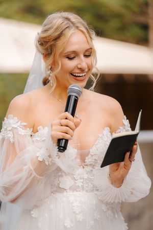 A series of candid photos showing a bride in a white lace dress with off-shoulder sleeves reading from a card at a wedding.