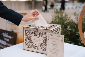 A decorative wooden wedding card box with intricate floral patterns being displayed at a reception venue.