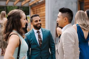 A small group of wedding guests in formal attire engage in conversation during an outdoor celebration.