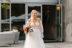 A bride in a white lace wedding dress stands in front of a modern building entrance.