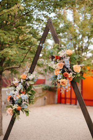 Floral arch decorated with peach roses and white flowers against a natural outdoor backdrop.