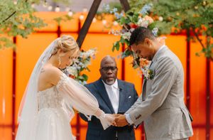 Wedding party poses in front of vibrant orange wall at outdoor garden venue during celebration.