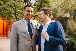 Two people in navy suits share a candid laughing moment during an outdoor photo session.