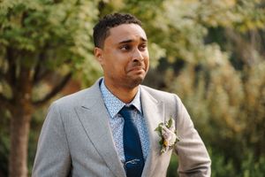 A wedding party stands in a garden setting wearing formal attire with gray suits and blue ties.
