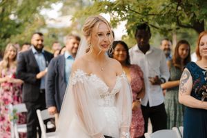 A wedding reception celebration outdoors with guests mingling under string lights and trees during golden hour.