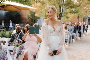 A romantic outdoor garden wedding ceremony features guests seated on wooden chairs along a stone path.