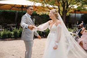 A joyful wedding couple dances together outdoors under autumn trees during their first dance celebration.