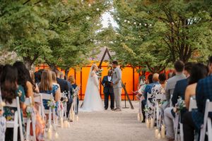 A panoramic view of visitors walking through an outdoor art installation with bright orange gates and green trees.