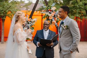 Wedding party celebrates joyfully outdoors with colorful orange decor and floral arrangements in the background.