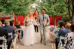 Wedding party walks through a lush garden pathway with trees and red temple gates in the background.