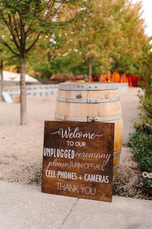 Wooden wine barrel signs displaying unplugged ceremony and welcome messages for a rustic outdoor wedding event.
