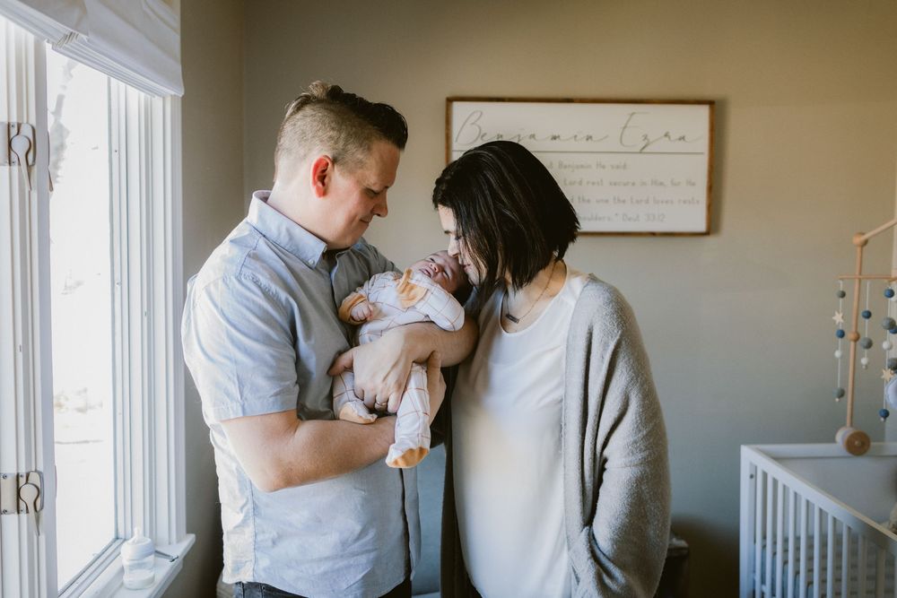 Husband and wife gaze at newborn in the nursery with a wooden sign in background for newborn photos. Manchester newborn photographer.