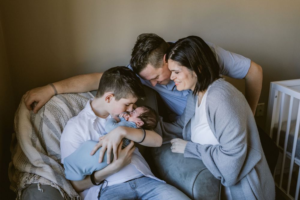 A family snuggles a newborn baby boy in his bedroom and look lovingly at him during an in-home newborn shoot in Haverhill, Massachusetts.