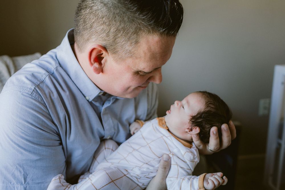 A father gazes happily at newborn son embracing his head during a newborn shoot in Haverhill, MA. Seacoast Dover newborn photographer.
