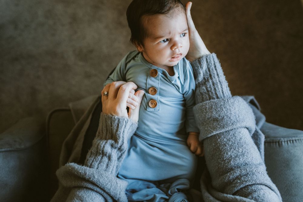 Newborn boy wearing a blue pajama gown looks lays on his mother's lap for newborn photos. Newburyport Concord newborn Photographer.