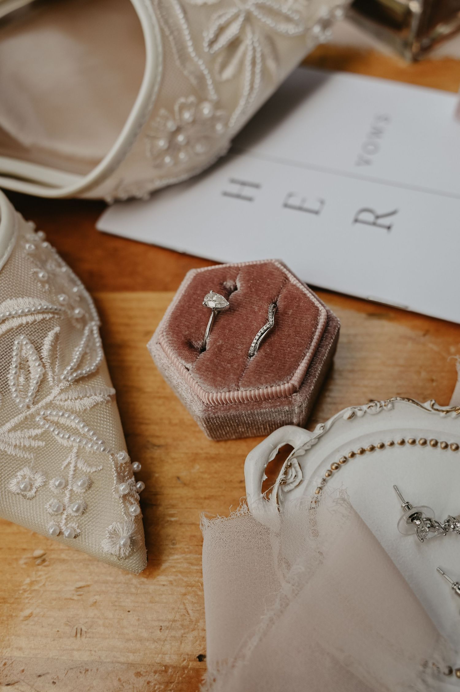 Wedding rings displayed in a velvet hexagonal box next to embroidered fabric and paper details.